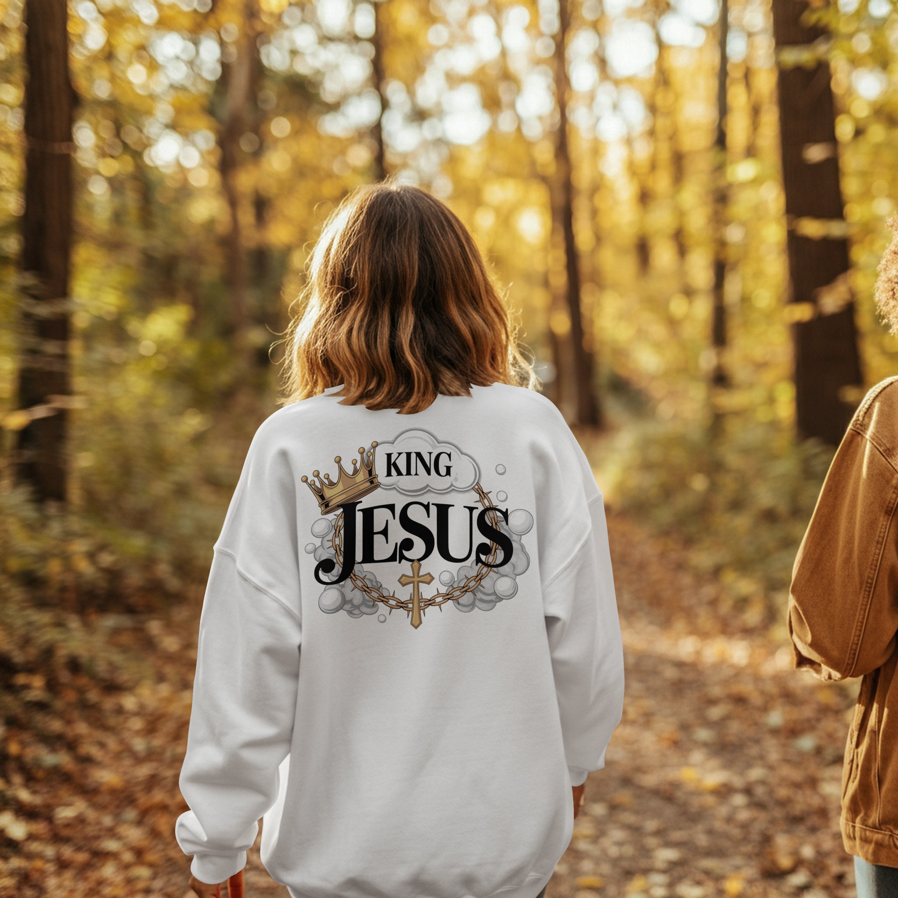 “Divine Faith Armor™ King Jesus Hoodie with crown, clouds, cross, and bold lettering design” Person wearing a sweatshirt with 'King Jesus' text in a forest setting